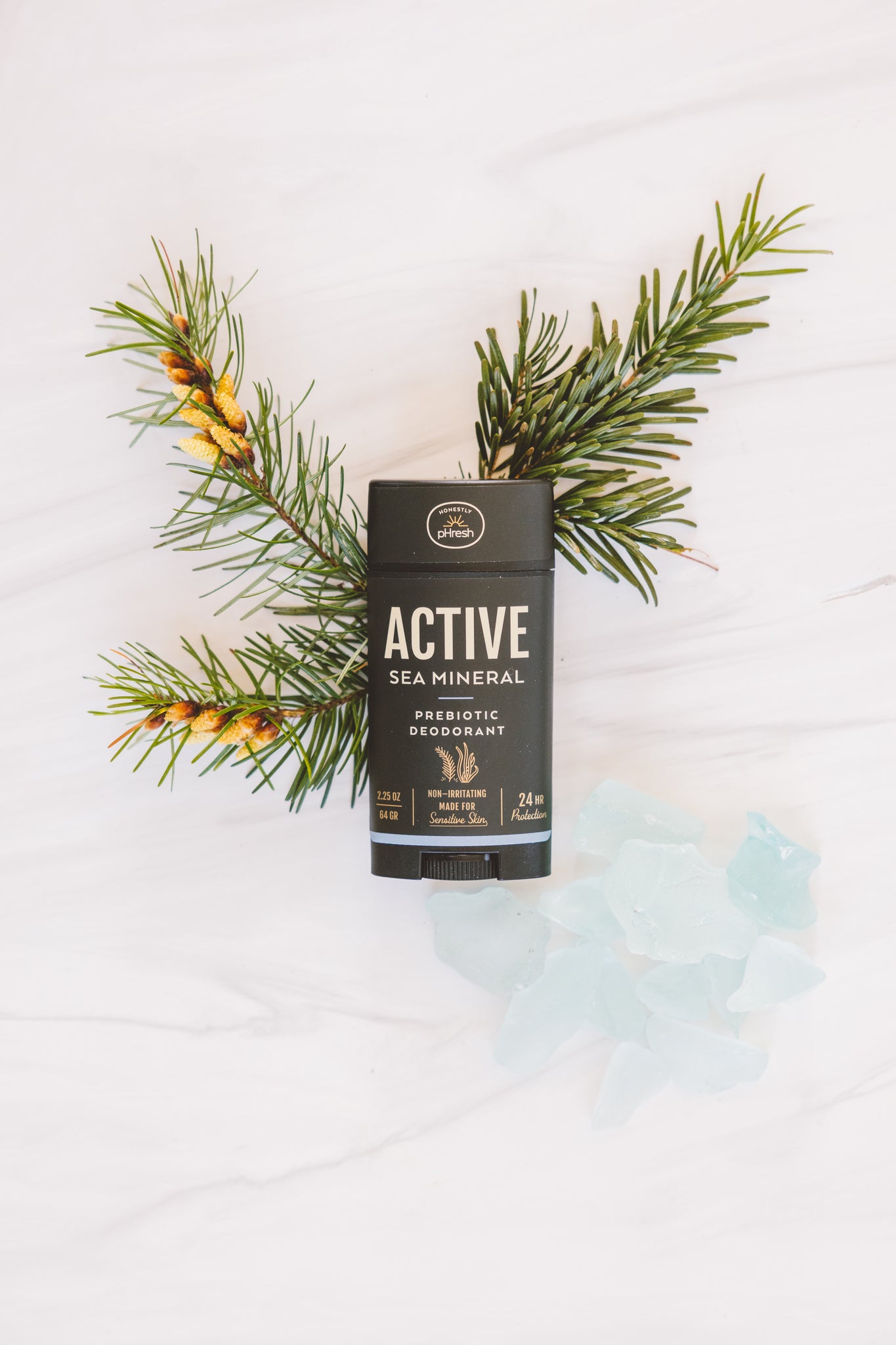 Active prebiotic deodorant stick featuring a sea mineral blend styled with pine & frosted glass pieces.